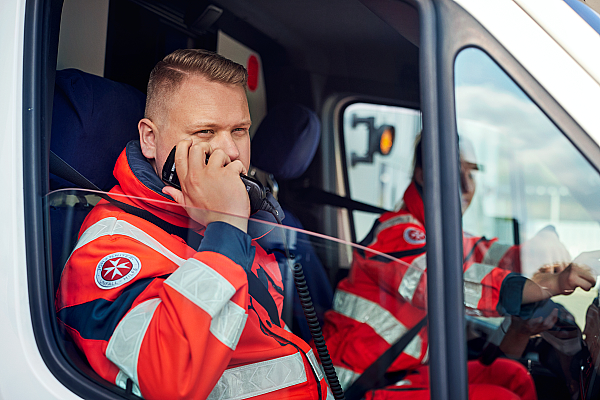 Johanniter in Einsatzkleidung im Rettungswagen, schaut aus dem Fenster und setzt einen Funkspruch ab