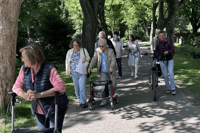 Menschen gehen auf einem Parkweg, zum Teil mit Rollator