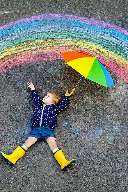 Kind mit Schirm unter einem gemalten Regenbogen
