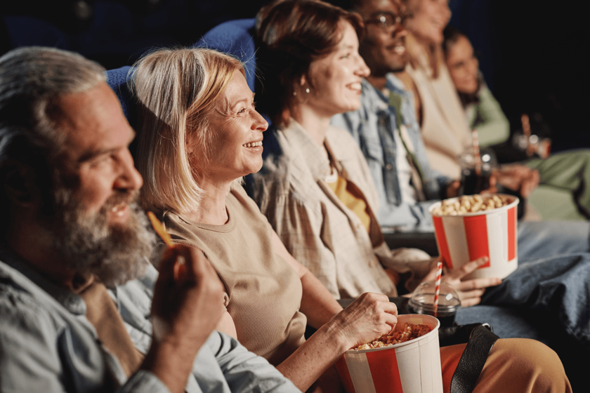 Mehrere Menschen sitzen lachend im Kino und essen Popcorn.