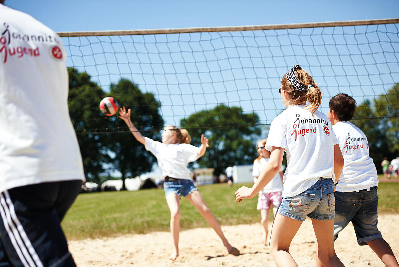 Mehrere junge Leute spielen Volleyball und tragen T-Shirts mit der Aufschrift "Johanniter Jugend"