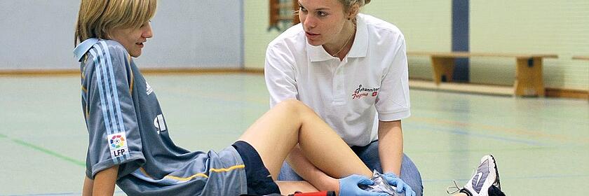 Schulsanitäterin kümmert sich um eine Schülerin nach einem Sportunfall.