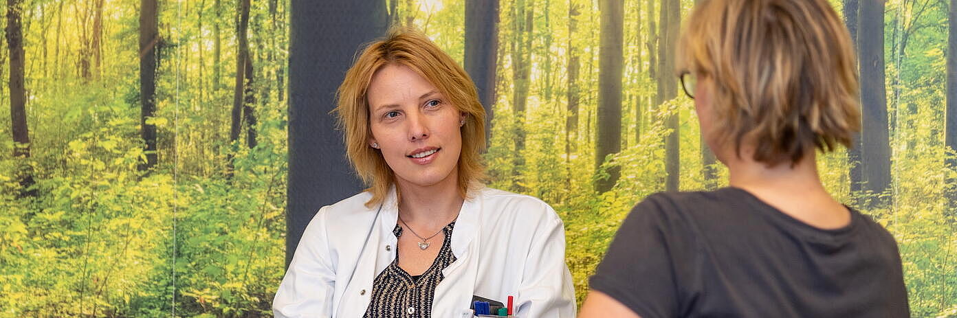 Ärztin bei einem Gespräch mit einer Patienten vor einer Waldtapete
