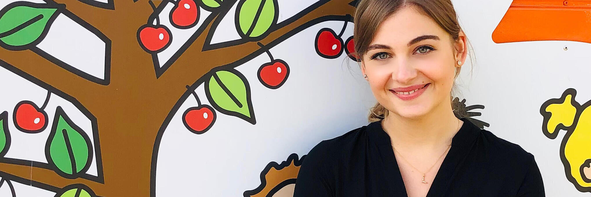 Linda, Leitung der Johanniter-Kita Kirschbaum vor einer Kirschbaum-Wand.