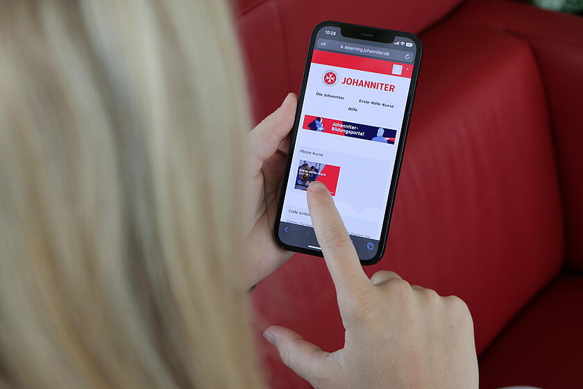 Person tippt mit dem Finger auf ein Smartphone mit rot-weißer App-Oberfläche.