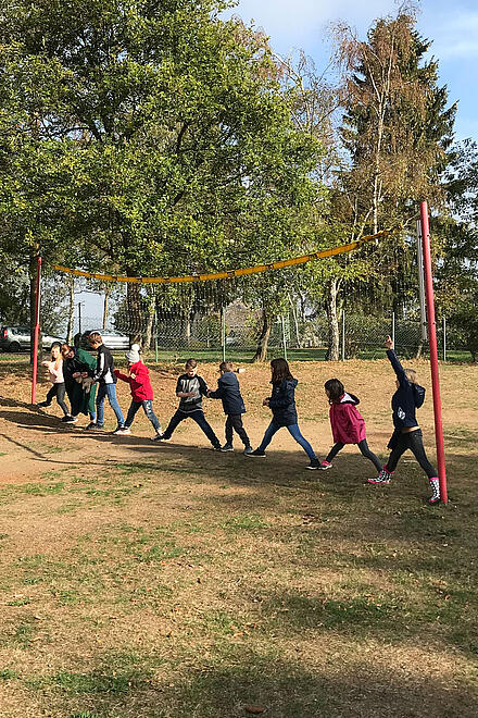 Kinder stehen in einer Reihe unter einem Volleyballnetz und spielen ein Spiel.