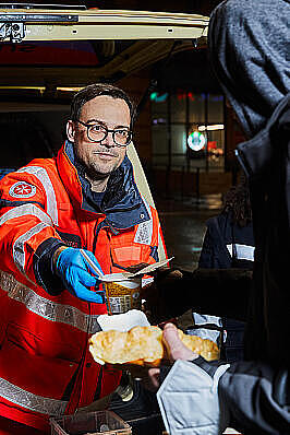 Ein Helfender des Kältebus gibt Essen an eine bedürftige Person aus