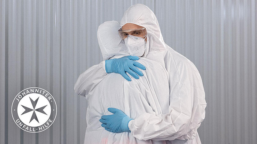 Zwei Personen in Schutzausrüstung während der Pandemie umarmen sich