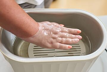 Eine Hand wird in flüssiges Paraffin getaucht.
